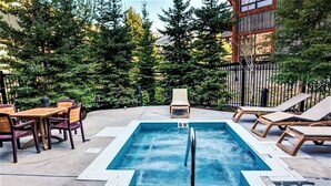 A rectangular outdoor pool with a metal ladder, surrounded by lounge chairs and a dining area with wooden tables and chairs. - 🥇Renovated 2BR, AC, Heated Pool, Hot Tub, Pets ok! (Canmore)