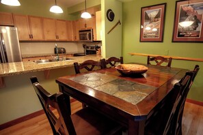 A kitchen with wooden cabinets, a stainless steel refrigerator, a microwave, and a dining table with a stone tile runner.