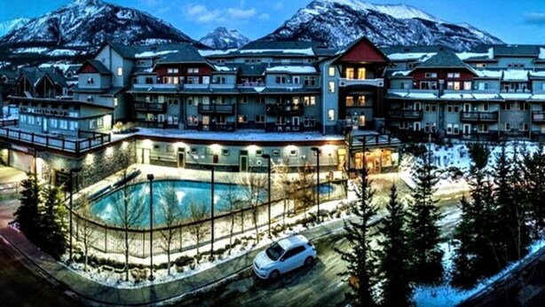 A large resort with multiple buildings, a swimming pool, and a mountainous backdrop. - 🥇Renovated 2BR, AC, Heated Pool, Hot Tub, Pets ok! (Canmore)