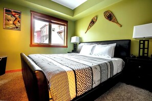 A bedroom with a large bed, a window, a nightstand, and a wall with two decorative items.