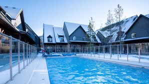 A swimming pool with a glass barrier, surrounded by buildings with snow-covered roofs. - 🥇Renovated Chalet at Mystic Springs, Pool, Hot Tub! (Canmore)
