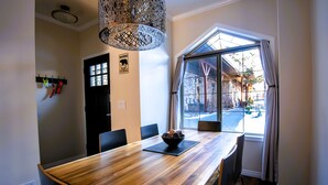 A dining area with a wooden table, chairs, a bowl of fruit, a hanging light fixture, and a window with curtains. - 🥇Renovated Chalet at Mystic Springs, Pool, Hot Tub! (Canmore)