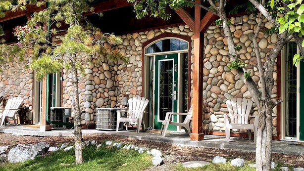 A stone building with a covered patio area, outdoor seating, and a stone wall. - 🥇Renovated Chalet at Mystic Springs, Pool, Hot Tub! (Canmore)