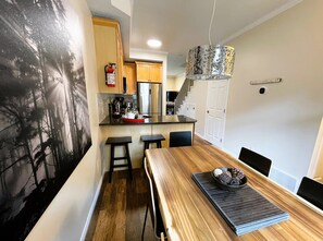 Eine moderne Küche mit Holztisch, Barhocker und einer Pendelleuchte.