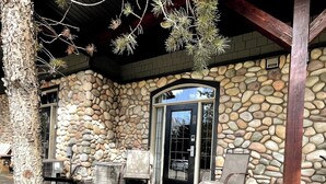 A stone building with a glass door, outdoor seating, and a tree. - 🥇Renovated Chalet at Mystic Springs, Pool, Hot Tub! (Canmore)