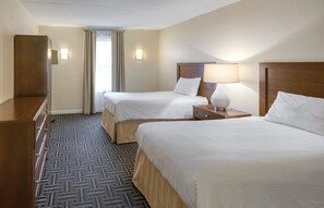 Habitación de hotel con dos camas, un aparador, una lámpara y un ventanal con cortinas.