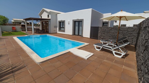 A modern pool area with a clear blue pool, white lounge chairs, and a stone wall. - Morning Star (Playa Blanca)