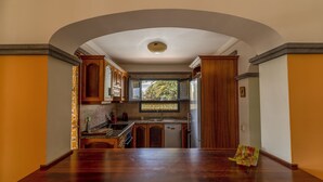 A kitchen with an archway leading to a dining area, wooden cabinets, a built-in oven, and a view of greenery outside. - Morning Star (Playa Blanca)