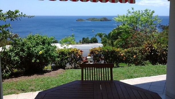 A covered patio with a view of the ocean and a small island. - GITES + SWIMMING POOL AND SPA, 5 Mn FROM MALENDURE BEACH AND VIEW OF THE PIGEON ISLANDS   (Bouillante)