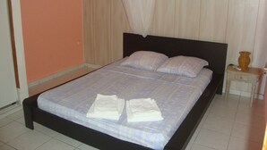 A neatly made bed with a headboard, a bedside table with a vase, and a plain wall. - GITES + SWIMMING POOL AND SPA, 5 Mn FROM MALENDURE BEACH AND VIEW OF THE PIGEON ISLANDS   (Bouillante)