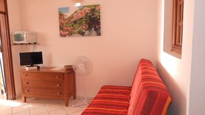 A room with a wooden dresser, a television, a fan, a sofa with a striped cushion, and a wall-mounted picture. - GITES + SWIMMING POOL AND SPA, 5 Mn FROM MALENDURE BEACH AND VIEW OF THE PIGEON ISLANDS   (Bouillante)