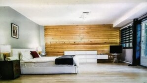 A modern bedroom with a wooden wall, a white bed, a bedside table, and a TV. - Chalet cheri (Mont-Tremblant)