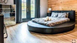 A modern bedroom with a curved bed, a wooden wall, and a large window. - Chalet cheri (Mont-Tremblant)