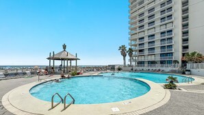 A pool area with a gazebo, lounge chairs, and a tall building in the background.