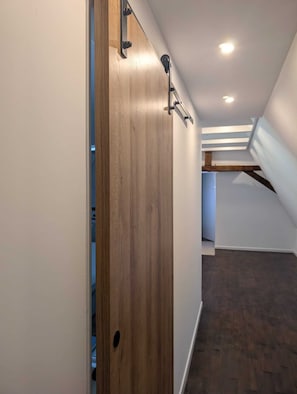 Un couloir avec une porte en bois, un plafond en pente et un espace mansardé visible.