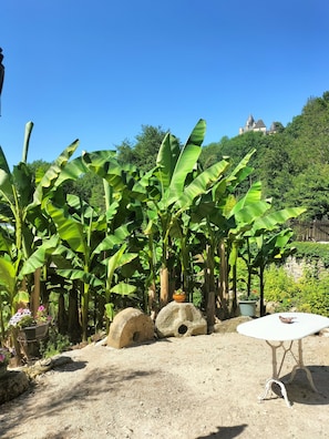 Un jardin avec des bananiers, une table blanche et une structure en pierre.