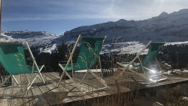 Uitzicht op een bergachtig landschap met een houten terras en groene stoelen gericht op het uitzicht.