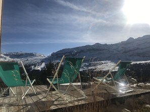 A view of a mountainous landscape with a wooden deck and green chairs facing the scenery.