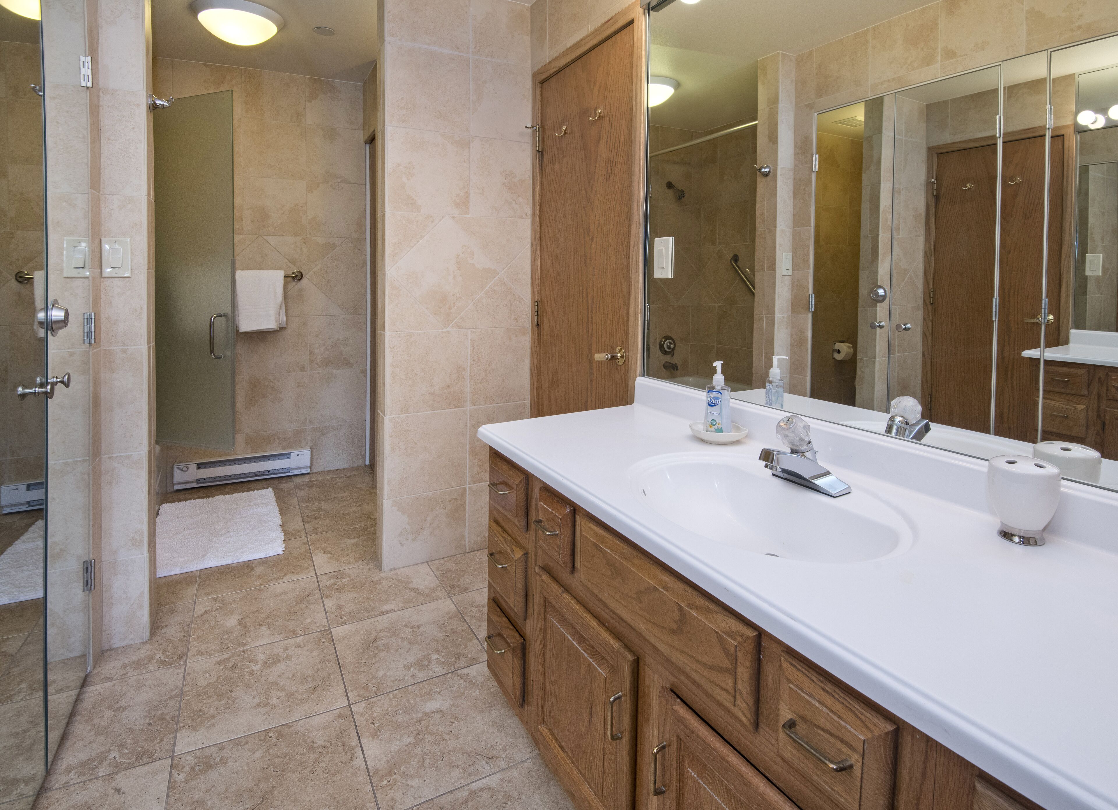 A modern bathroom with a large mirror, two sinks, wooden cabinets, and a shower area.