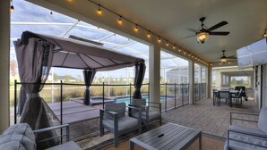Un patio cubierto con mobiliario exterior, piscina y una pantalla de televisión.