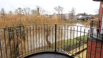 A view from a balcony overlooking a river with a metal railing and a brick building in the background.