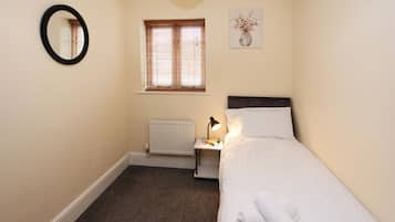 Een slaapkamer met een bed, een nachtkastje met een lamp, een radiator, een raam met jaloezieën, een spiegel aan de muur en een schilderij.