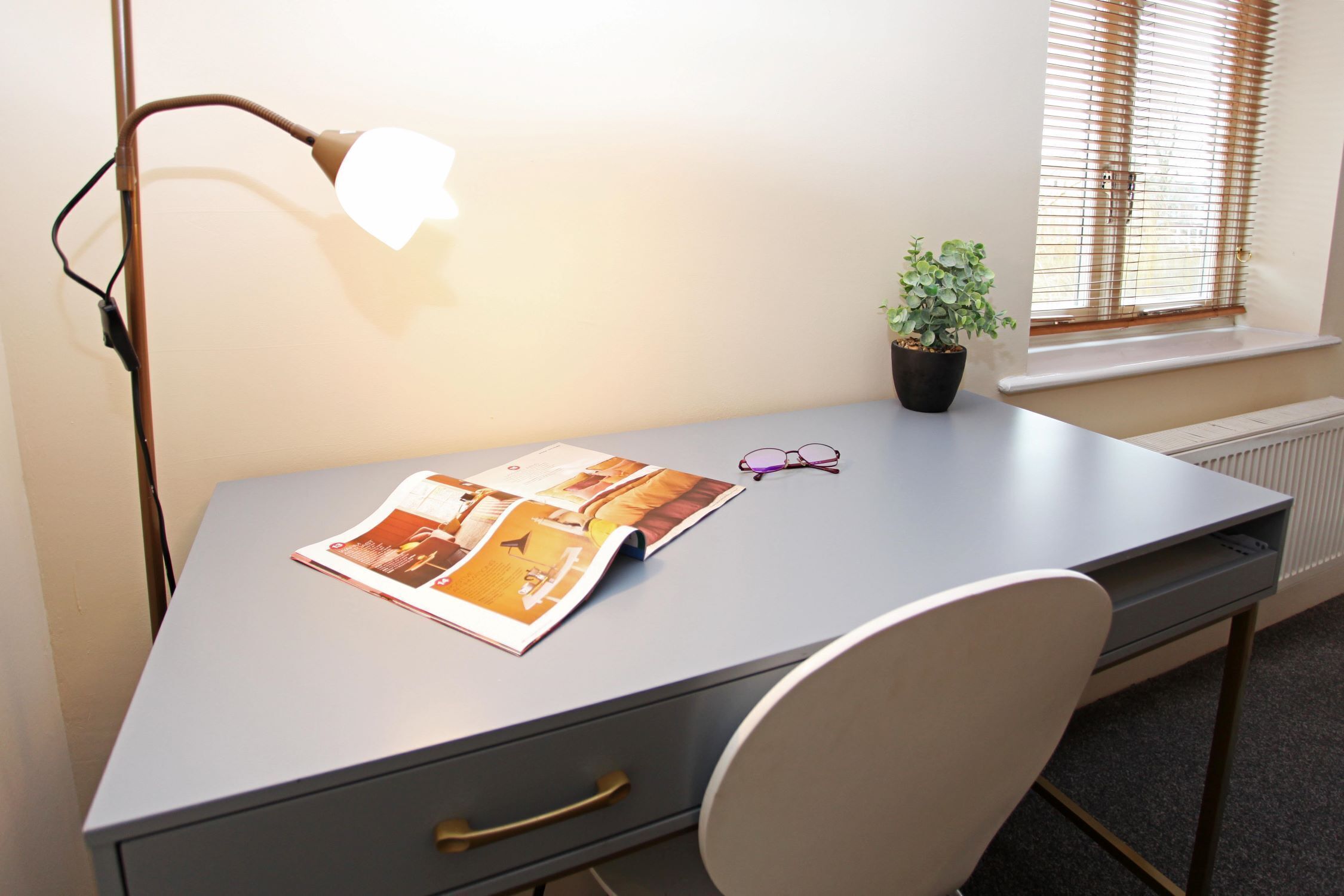 A desk with a lamp, a pair of glasses, and a plant.