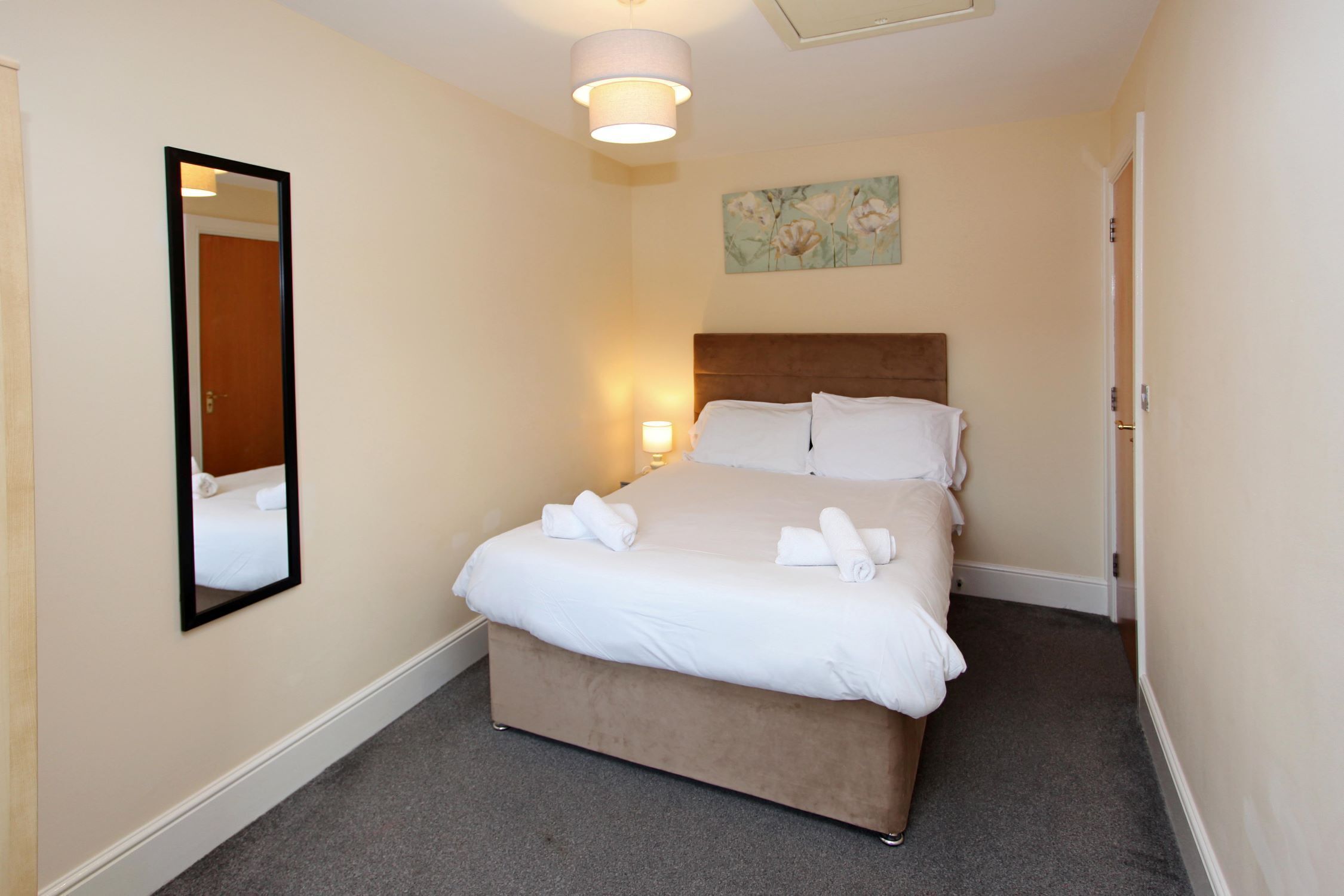 Habitación de hotel con una cama grande, una lámpara de noche, un espejo y un cuadro en la pared.