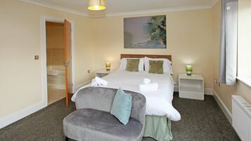 A hotel room with a bed, a grey armchair, a painting on the wall, and a window with curtains.