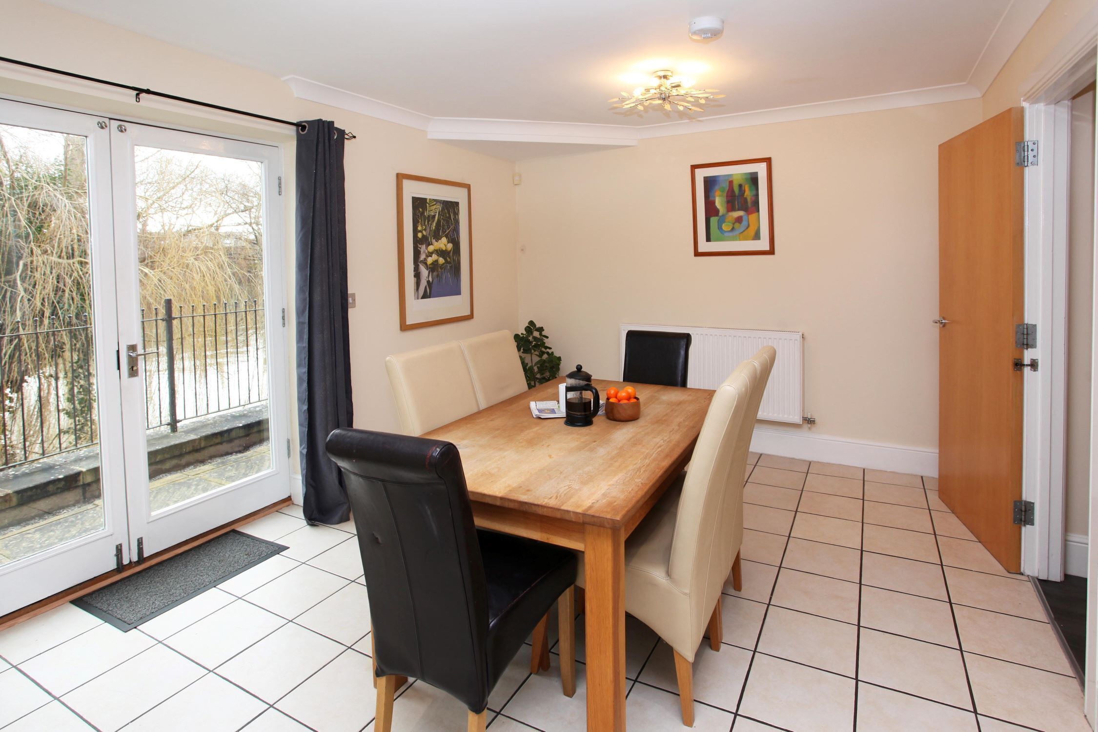 A dining area with a wooden table, four chairs, a radiator, and two framed pictures on the wall.