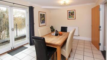 A dining area with a wooden table, four chairs, a radiator, and two framed pictures on the wall.