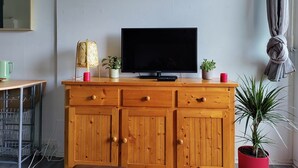 A living room with a wooden cabinet, a television, a painting, and a potted plant. - Oceanfront studio above the pines (Seignosse)