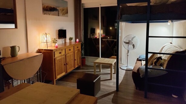 A cozy living room with a wooden cabinet, a small table, a couch, and a fan. - Oceanfront studio above the pines (Seignosse)