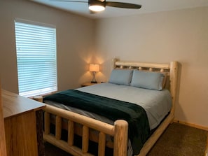 A bedroom with a wooden bed frame, a nightstand with a lamp, and a ceiling fan.
