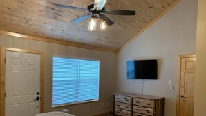 A bedroom with a bed, a dresser, a ceiling fan, a window with blinds, and a TV mounted on the wall. - Cozy Cabin with Modern Amenities (Pet Friendly) (Pagosa Springs)