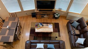 A living room with a brown leather sofa, a wooden coffee table with a guest book, a flat-screen TV, and a dining area with a wooden table and chairs. - Cozy Cabin with Modern Amenities (Pet Friendly) (Pagosa Springs)
