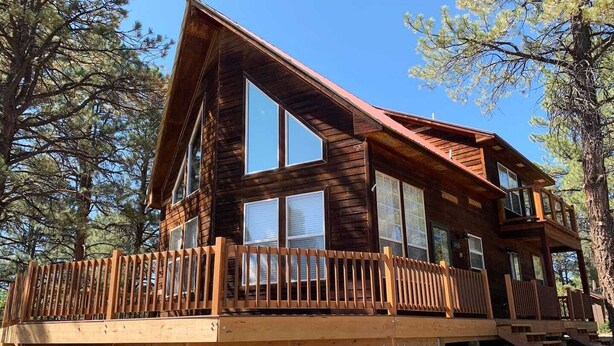 A wooden cabin with large windows, a deck, and a staircase leading to the upper level. - Cozy Cabin with Modern Amenities (Pet Friendly) (Pagosa Springs)