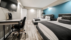 Hotellihuone, jossa on työpöytä, kaksi sänkyä, televisio ja tuuletin.