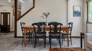 Un comedor con una mesa de madera y cuatro sillas, un espejo en la pared y un cuadro enmarcado.