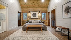 A bedroom with a large bed, a wooden ceiling, and two windows.