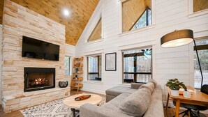 A cozy living room with a fireplace, a grey sofa, a coffee table, and a wooden desk with a lamp.