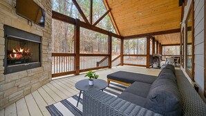 A covered outdoor area with a stone fireplace, a black sofa, and a small table with a plant.