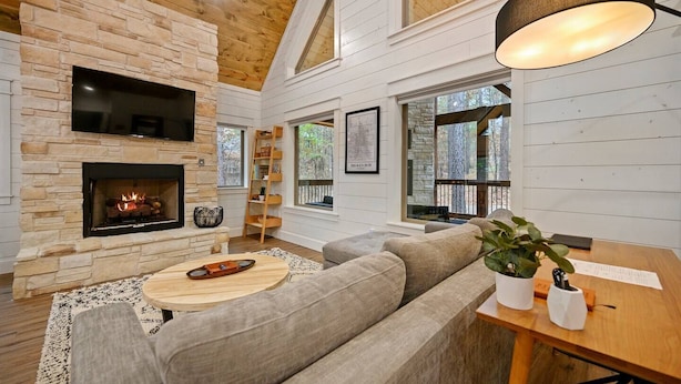 A cozy living room with a stone fireplace, a large window, and a wooden ceiling.