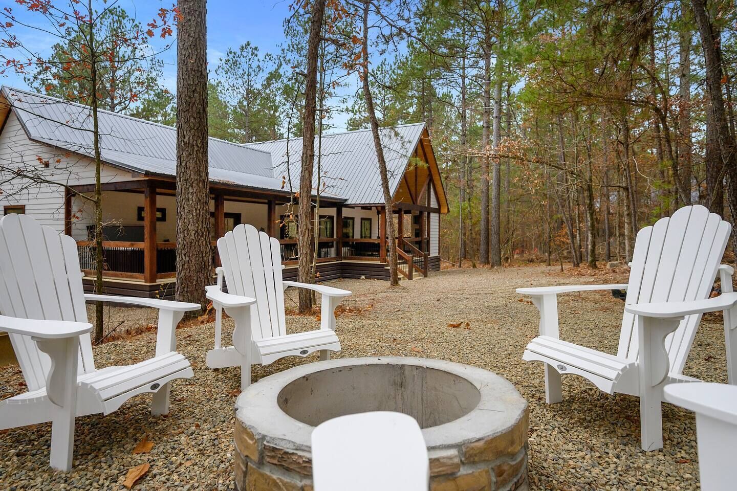 Een blokhut met een vuurkorf van steen en witte Adirondack-stoelen, gelegen in een bos.