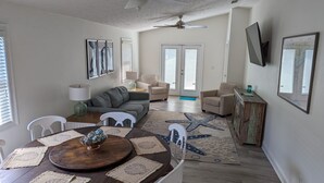 Amplia sala de estar con un sofá gris, sillones color beige, una mesa de centro de madera con un cuenco decorativo, y un tapiz grande con estampado de estrellas de mar.