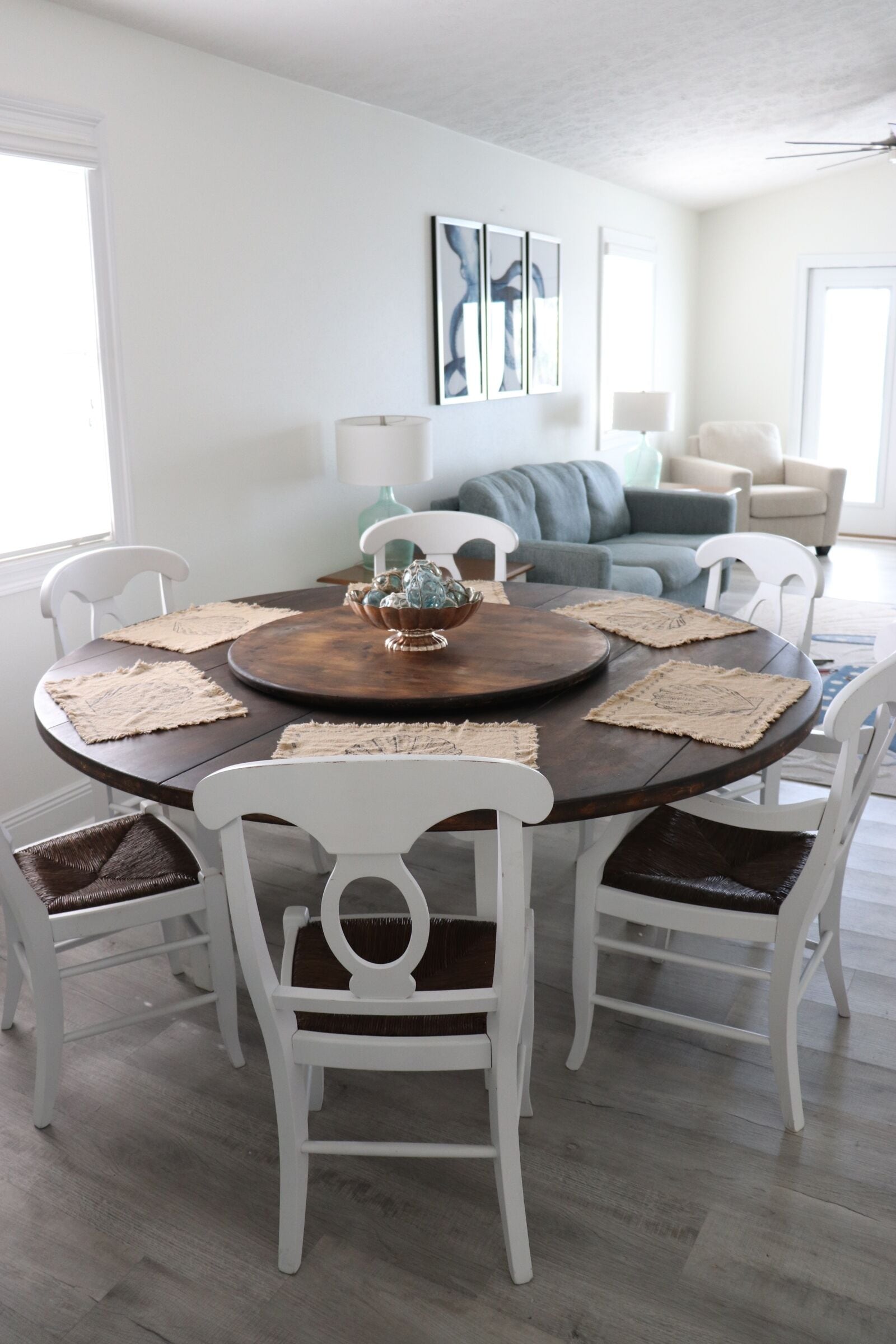 Un coin repas avec une table ronde en bois, des chaises blanches et des sets de table en fibres tressées.