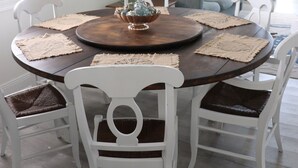 Un comedor con una mesa redonda de madera, sillas blancas y protectores de mesa tejidos.