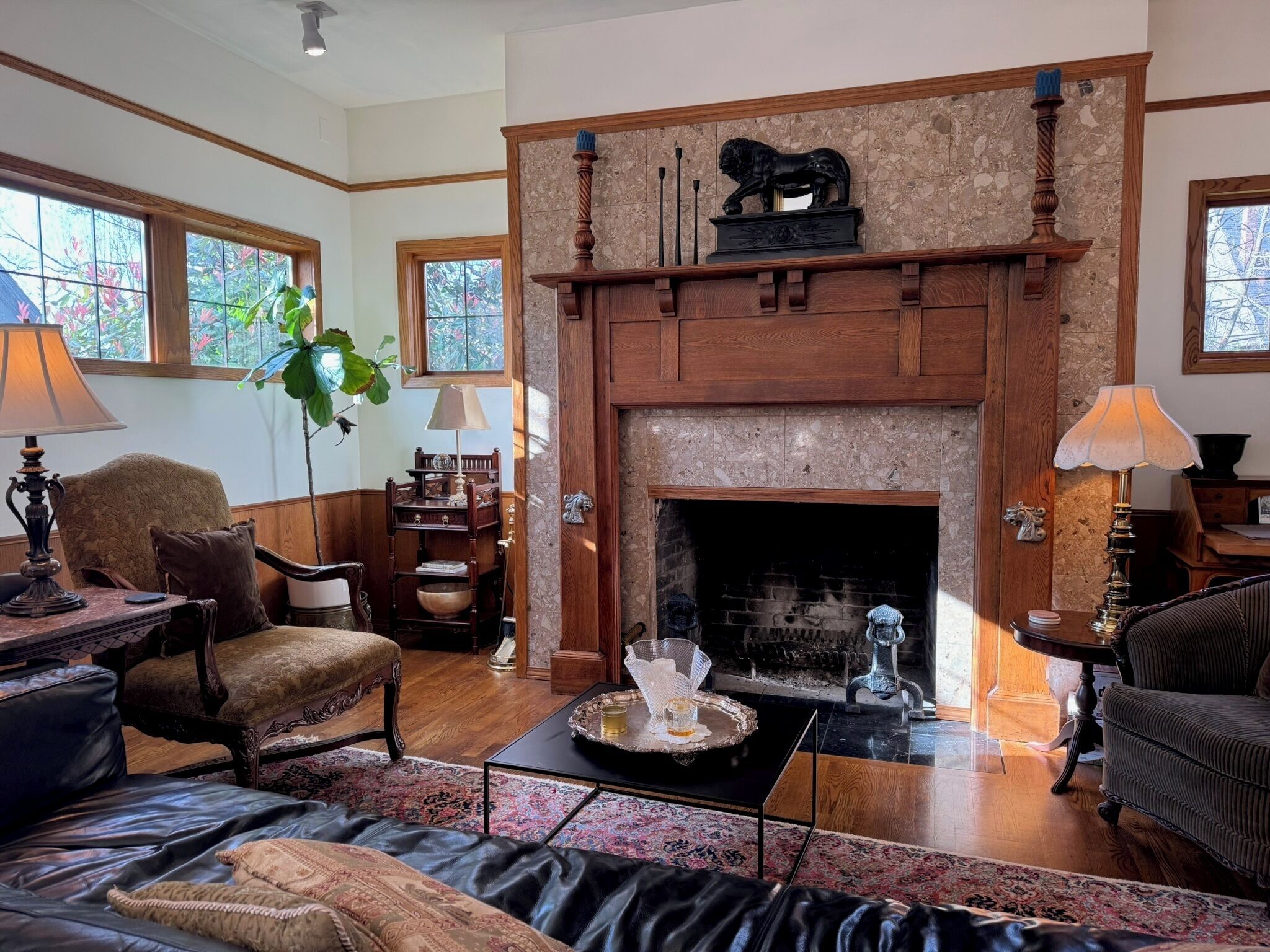 A cozy living room with a fireplace, wooden furniture, and a large window.