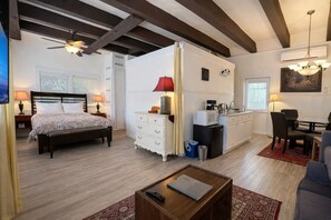Un dormitorio con cama, mesitas de noche, escritorio, silla, kitchenette pequeño y zona de comedor con mesa y sillas.
