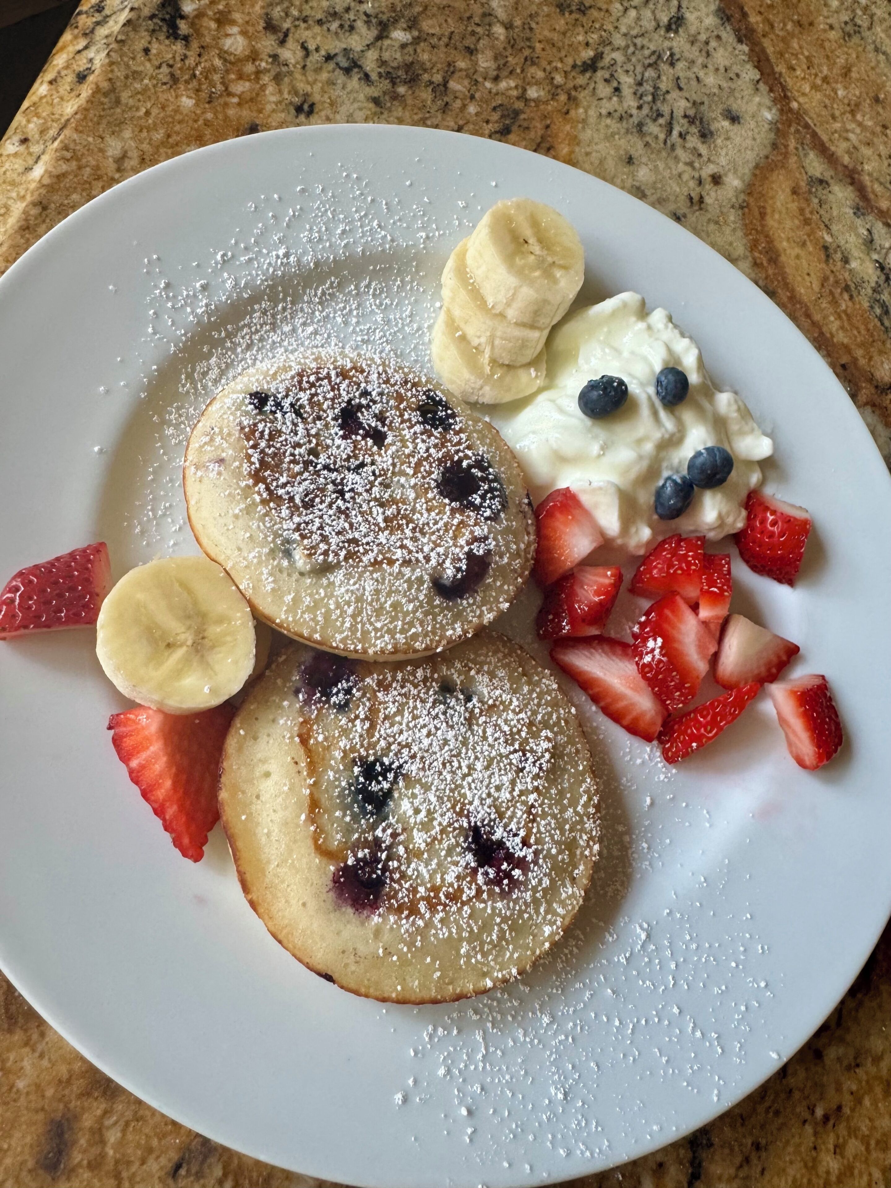 A plate with pancakes, strawberries, blueberries, banana slices, and whipped cream.